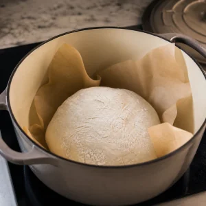 Unbaked gluten-free sourdough lowered on parchment into a hot Dutch oven