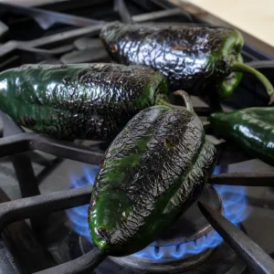 Poblano peppers blistering over blue gas flames on a stovetop.