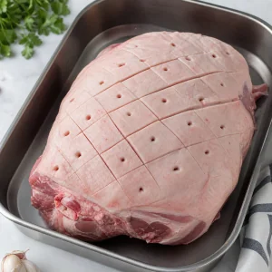 Raw pork shoulder scored in a diamond pattern in a roasting pan