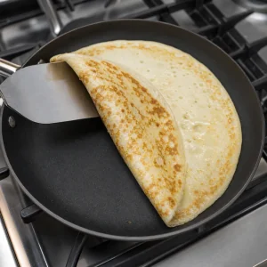 Dutch pancake flipped with a wide spatula showing golden brown spots