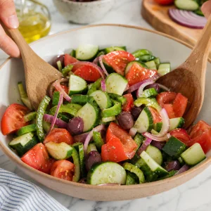 Greek salad vegetables gently tossed with wooden spoons to coat in dressing.