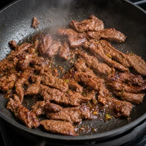 Marinated beef searing in a single layer until browned