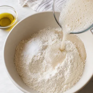 Foamy yeast mixture and olive oil poured into bread flour and sea salt