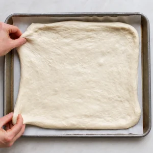 Pizza bianca dough stretched across a parchment-lined rimmed baking sheet