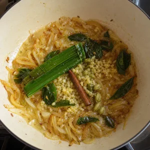 Ginger, garlic, curry leaves, pandan, cinnamon, and cardamom frying with onions.
