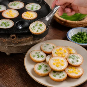 Warm khanom khrok pancakes lifted from the pan and placed onto a serving plate