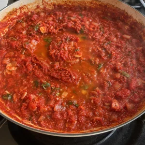 Tomatenmark und Weißwein köcheln zu einer dickeren Tomatensauce ein
