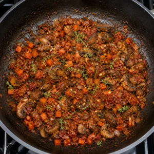 Tomato paste and herbs stirred into mushrooms and vegetables