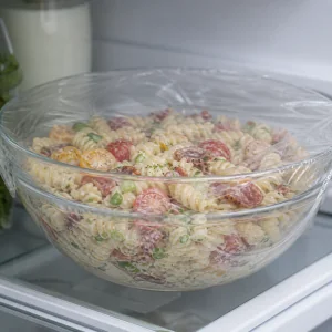 Abgedeckte Schüssel mit Nudelsalatmischung kühlt vor dem Servieren