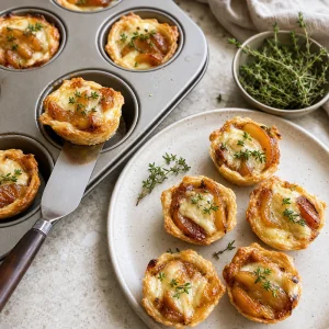 Bites de tarte Tatin com brie e maca finalizados, decorados com tomilho fresco e retirados da forma de muffin para servir quentes