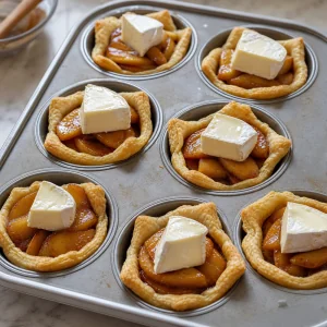 Copos de massa folhada recheados com macas caramelizadas e cobertos com pedacos de brie antes de assar