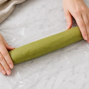 Matcha shortbread dough shaped into a log on plastic wrap
