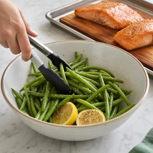 Raw green beans and lemons tossed beside resting salmon