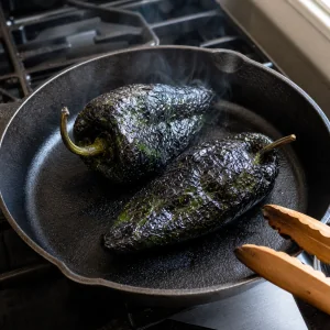Poblano peppers blistering in a cast-iron skillet