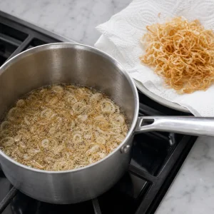 Thinly sliced shallots frying in oil until pale golden