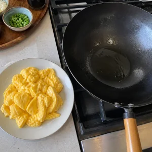 Cooked egg curds set aside beside an oiled wok