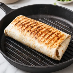 Rolled burrito crisping seam-side down on a grill pan