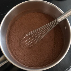Dry cocoa mixture in a saucepan with a whisk