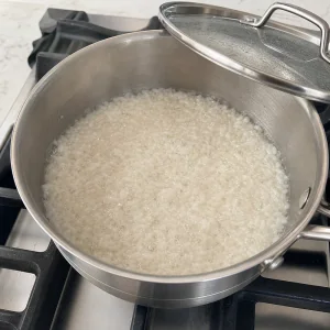 Arroz a cozinhar com água numa panela até o líquido ficar quase absorvido.