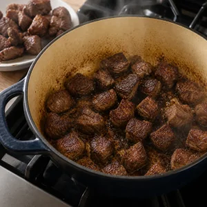Beef cubes browning in a Dutch oven until deeply seared.