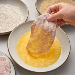 Floured pork cutlet dipped into beaten eggs with excess dripping off.