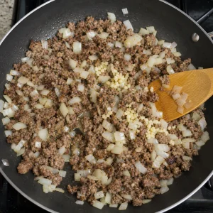 Diced onion and minced garlic stirred into browned meat for lasagna