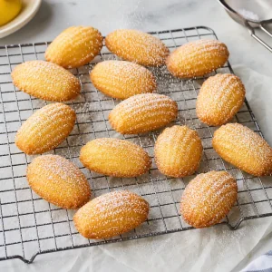 Warm madeleines on a wire rack dusted with powdered sugar