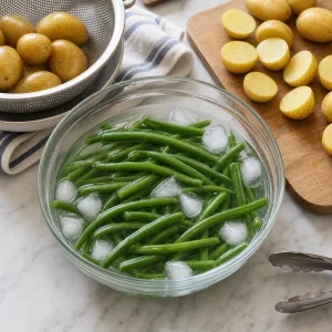 Blanched haricots verts chilled in ice water with halved potatoes nearby