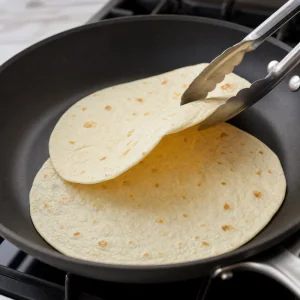 Flour tortillas warming in a dry skillet until soft and pliable.
