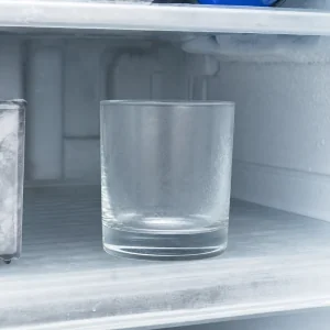 Empty rocks glass chilling on a frosty freezer shelf