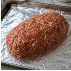 Raw meatloaf shaped into a neat loaf on a foil-lined baking sheet