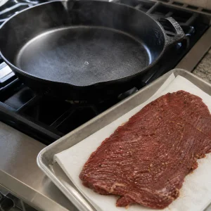 Heiße leere Gusspfanne neben einem trocken getupften marinierten Flanksteak