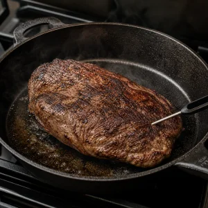 Ganzes Flanksteak beim Anbraten in einer Gusspfanne mit eingestecktem Thermometer