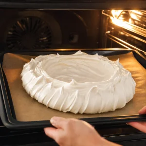 Shaped pavlova meringue baking on parchment in the oven until firm and dry.