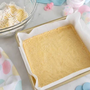 Shortbread crust pressed into a parchment-lined pan for lemon bars