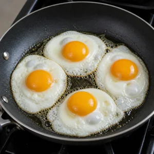 Four eggs frying with set whites and soft yolks