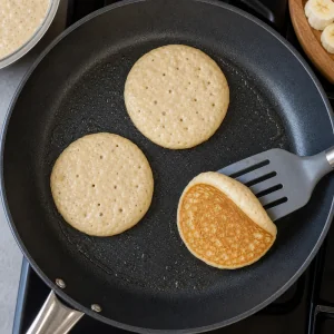 Panqueques cocinándose con bordes firmes, burbujas arriba y una base dorada visible.