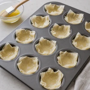 Cuadrados de masa filo presionados en moldes de mini muffins y pincelados con mantequilla.