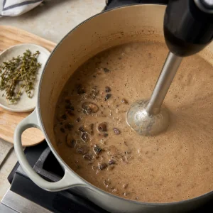Stabmixer pueriert Pilzsuppe nachdem die Thymianzweige entfernt wurden