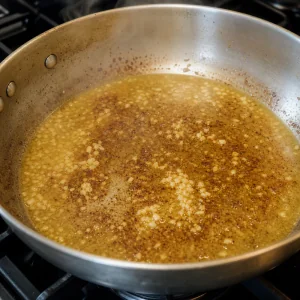Alho picado e caldo de frango soltando pedacos dourados da frigideira