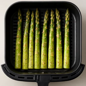 Seasoned asparagus arranged in a single layer in an air fryer basket.