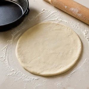 Small round of pizza dough stretched on a floured surface