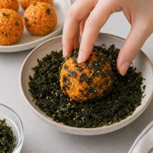 A kimchi rice ball being rolled in crushed roasted seaweed flakes.