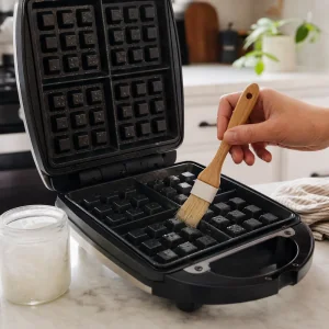Open waffle iron being lightly greased with coconut oil.
