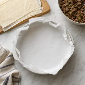 Round baking dish lined with parchment paper for phyllo meat pie