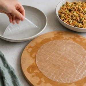 Translucent rice paper softening beside a shallow dish of warm water