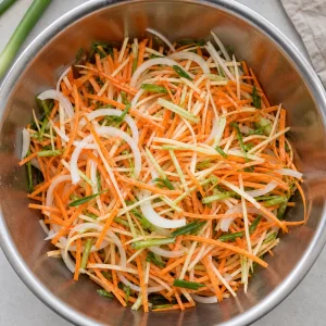 Raw vegetable strands tossed together in a mixing bowl.