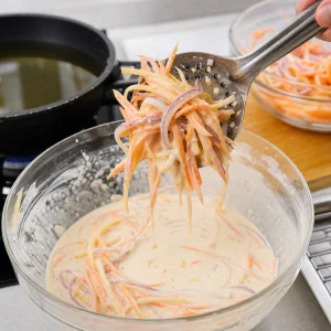 A slotted spoon lifts a battered vegetable bundle while excess batter drips off