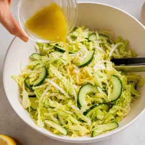 Lemon olive oil dressing poured over Napa cabbage and cucumber salad