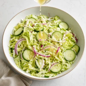 Light dressing being drizzled over Napa cabbage, cucumber, and red onion salad.